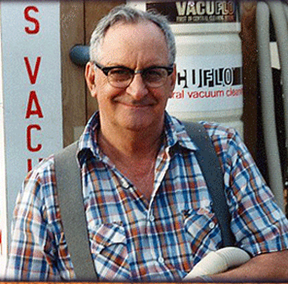 Founder Oakley Mr. Oaks O'Bryan smiling in front of the Oaks Vacuum shop sign beside a VacuFlo central vacuum power unit