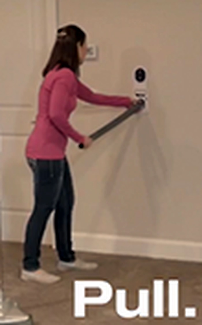 A woman pulling the retractable Hide-A-Hose hose out of a wall inlet in a hallway