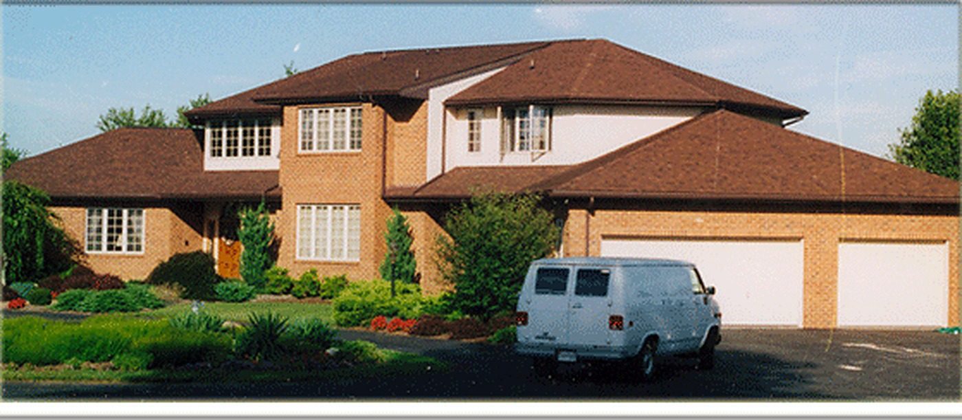The A Plus Oaks white service van parked in the driveway of a large brick two story home during a central vacuum installation